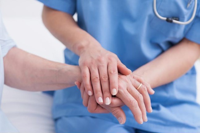 A nurse and patient hold hands.