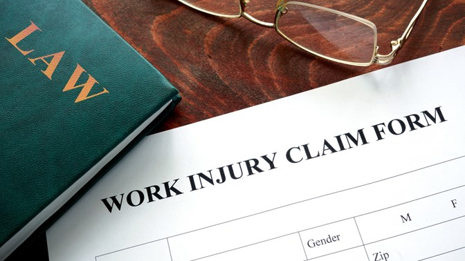 Work injury claim form on a desk with a law book and eye glasses as part of the workers compensation program.
